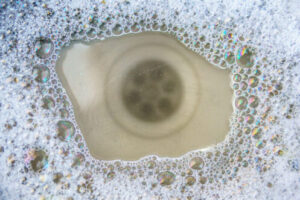 Close-up view of a drain opening surrounded by soap bubbles and foam, showing the interior pipe structure during cleaning process.