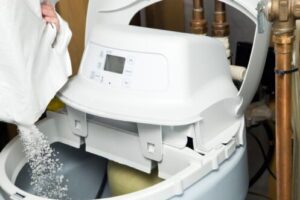 White water softener tank with digital control panel being filled with salt pellets during maintenance.