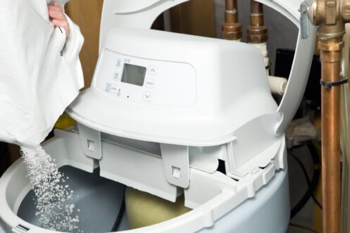White water softener tank with digital control panel being filled with salt pellets during maintenance.