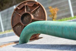 Green corrugated drainage pipe and rusty metal sewer access cover on concrete ground with construction materials visible in background.