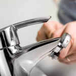 Close-up of hands adjusting a chrome bathroom faucet with an adjustable wrench during repair or installation work.