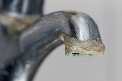 Close-up of mineral limescale and calcium deposits accumulated on a chrome faucet aerator and spout.