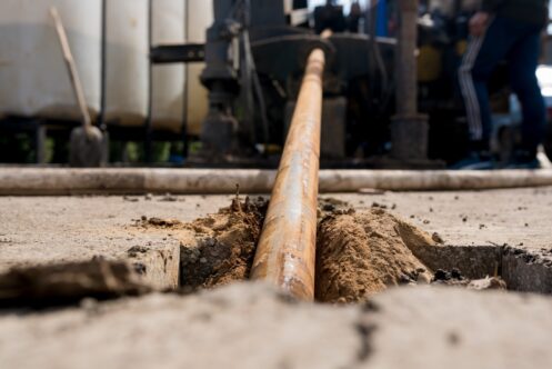 Close-up view of a wooden pipe or conduit partially buried in soil during underground pipeline installation or lining work.