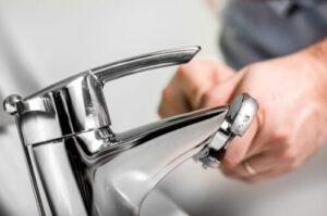 Person adjusting a chrome bathroom faucet with a wrench during plumbing repair work.
