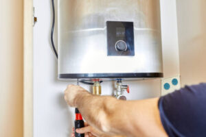 Technician adjusting valve on white tankless water heater mounted on wall with control panel visible.