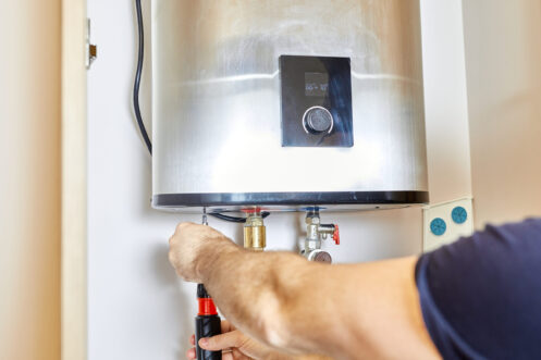Technician adjusting valve on white tankless water heater mounted on wall with control panel visible.