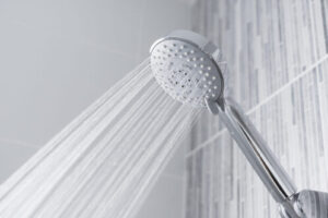 Modern chrome showerhead dispensing multiple streams of water against a white tile bathroom wall.