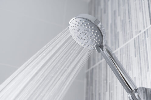 Modern chrome showerhead dispensing multiple streams of water against a white tile bathroom wall.