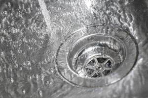 Close-up view of water swirling down a metal sink drain with visible drain cover and splashing water droplets.