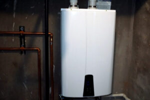 White cylindrical tankless water heater mounted on wall with copper piping connections and black base.