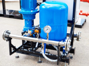 Industrial blue vertical turbine pump with motor, pressure gauge, metal frame base, and connecting pipes on concrete floor.